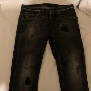 Svarta  jeans från Dondup - Snygga svarta skinny jeans från Dondup, modell George Skinny Fit. Jeansen har slitna detaljer och hål för en cool, edgy look. Klassisk femficksmodell med diskret D-logga på bakfickan. Tillverkade i stretchig denim för skön passform. Det är i storlek w29 och nypris för detta paret är cirka 4500 mitt pris 799kr vid en snabb och enkel affär kan ta emot byten om de är andra dondups.