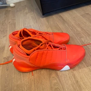 Hardens 7  - Hardens 7 storlek 46,Feta oranga sneakers från Adidas med cool design och tydliga ränder på sidan. Skorna har snörning, rund tå och en chunky sula med vita detaljer. Ovandelen är i textil och syntet, perfekt för dig som vill sticka ut med färg.