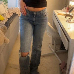 Blå raka jeans med hål på knät - Säljer ett par blå jeans med rak passform och snyggt hål på ena knät. Jeansen har klassisk femficksdesign, normal midja och är i ett mjukt denimtyg. Perfekta för en avslappnad och trendig look.