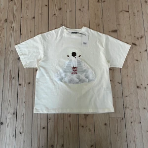 Vit Yeti t-shirt från MOIST-IJustWantToBeCool - Vit t-shirt från MOIST från IJustWantToBeCool med ett stort grafiskt tryck framtill på Yeti i vitt på en trappa bland moln som lyser i mörkret. Oversize i passformen så lite stor. Materialet är mjuk bomull, perfekt för en clean och cool look. Ny med prislapp och kartong!