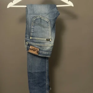 Blå Slim jeans från Lee Luke W30 L34 - Snygga blå Lee Luke jeans i Slim fit med klassisk femficksdesign och slitna detaljer. Jeansen har en mörk tvätt med ljusa partier och Lee-logga på bakfickan. Perfekta för dig som gillar en smal siluett och stilren look.