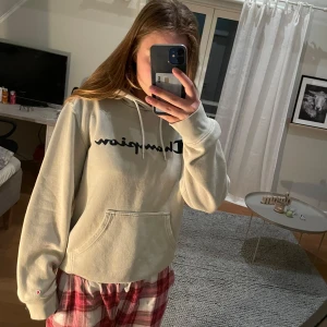 Beige hoodie från Champion  - Säljer en beige hoodie från Champion i storlek M. Tröjan har svart Champion-logga på bröstet, huva med snörning och en stor magficka. Säljer på grund av att den inte kommer till användning💖