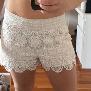 Vita spets-shorts från Gina Tricot - Superfina vita shorts från Gina Tricot med bred resår i midjan med ett spets mönster i ”virkat” material. De är använda men finns inga tydliga tecken på det. De är i storlek 40 men passar dig som brukar ha S.  Hör av er vid funderingar!😊🤍