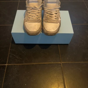 Vita och grå sneakers från Philippe Model - Snygga sneakers från Philippe Model i vitt och grått med klassisk design. Skorna har snörning, rund tå och detaljer i både skinn och mocka. Perfekta för dig som gillar en stilren och sportig look. Sulan är platt och har fiskbensmönster undertill.