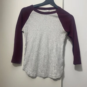 Grå och vinröd långärmad tröja H&M - Snygg långärmad tröja från H&M Divided i storlek S. Tröjan har grå bas och vinröda ärmar med raglanmodell och rund halsringning. Perfekt för en chill och avslappnad stil. Tillverkad i mjuk bomull som känns skön mot huden.