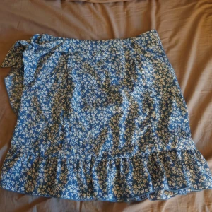 Blå blommig kjol med volang - Söt blå kortkjol med volang från shein, perfekt nu till sommaren. Används ett par gånger, finns ett litet hål men de syns knappt när man har på sig den