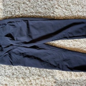 Svarta kostymbyxor från IKRA - Svarta kostymbyxor från IKRA i klassisk rak modell. Byxorna har en stilren look med normal passform och är perfekta för dig som gillar en clean och enkel stil. Materialet känns mjukt och följsamt, vilket gör dem bekväma hela dagen.