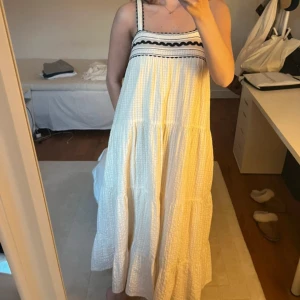 Beige långklänning med svarta detaljer - Otrolig beige långklänning med svarta vågiga band och broderade detaljer upptill. Har underklänning. 🤍 nyskick