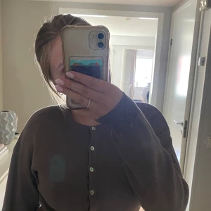 Brun kofta från Gina Tricot - Mysig brun kofta från Gina Tricot med rund halsringning och vita knappar framtill. Tröjan är stickad i mjukt material och har långa ärmar samt breda ribbade muddar vid ärmslut och nederkant, tröjan är lite kort i modellen. Perfekt för lager-på-lager och chill vibes.