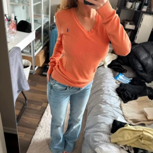 Orange v-ringad tröja Polo Ralph Lauren ÄKTA!  - Säljer en orange v-ringad tröja från Polo Ralph Lauren med blå logga på bröstet. Tröjan är i mjuk bomull, har långa ärmar och ribbade muddar. Perfekt för dig som gillar klassisk stil med en färgklick. ÄKTA SÅKLART!!!! 