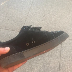 Svarta loobs du får dom hellt rena dom ör bara smutsiga nu. - Svarta sneakers i mocka från Louboutin med coola silverfärgade nitar på tån och röd sula med logga. Skorna har snörning och rund tå, samt svarta detaljer och metallhål på sidan. Perfekt för dig som vill sticka ut med en edgy vibe. 