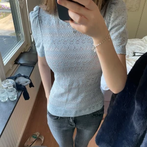 Ljusblå spetsblus från Vila❣️ - Supersöt ljusblå blus från Vila med kort puffärm och rund hals. Blusen är täckt av ett detaljerat spetsmönster och har en feminin, figurnära passform. Perfekt att styla med jeans eller kjol för en fräsch look.💕