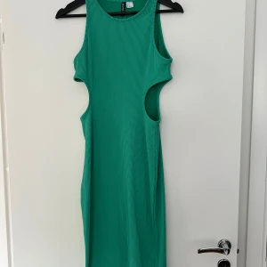 Grön ribbad klänning från Divided - Snygg grön ribbad klänning från Divided med cut-out detaljer i sidorna. Ärmlös modell med rund halsringning och figurnära passform. Perfekt för dig som vill sticka ut med en cool och modern look.