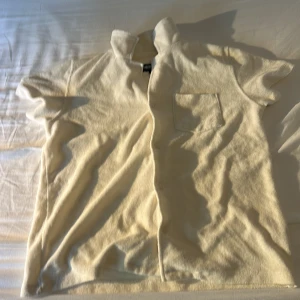 Beige frottéskjorta från Nikben - Säljer en beige kortärmad skjorta från Nikben i mjuk frotté. Skjortan har klassisk krage, knäppning framtill och en bröstficka. Perfekt för chill dagar eller strandhäng. Enkel och stilren design som är lätt att matcha. 