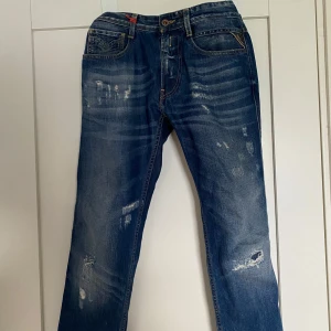 Replay jeans, blå, storlek 32/34 - Säljer ett par blå Replay jeans med slitna detaljer och snygg tvätt. Klassisk femficksmodell med läderpatch bak i midjan och kontrastsömmar. Jeansen har raka ben och normal passform, tillverkade i bomull. Perfekta för en avslappnad streetstil.