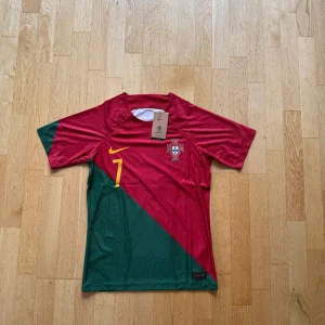 Portugal Ronaldo fotbollströja Nike S - Portugal landslagströja från Nike med Ronaldo och nummer 7 på ryggen. Tröjan är röd och grön med gula detaljer, kortärmad och tillverkad i lätt funktionsmaterial. Landslagsemblem på bröstet och snygg diagonal design framtill.