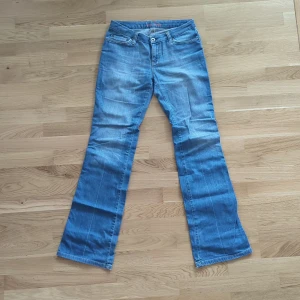 Blå bootcut jeans från Vero Moda - Snygga y2k ljusblå bootcut jeans från Vero Moda med klassisk femficksdesign och broderade bakfickor och lång midja. Jeansen har normal passform och är tillverkade i mjukt denimtyg. Tyget längs ner vid hälen är lite skavt.