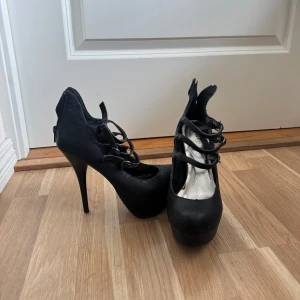 Svarta pumps med snörning och platå - Snygga svarta pumps med hög klack och platåsula. Skorna har flera remmar med snörning framtill och dragkedja bak. 