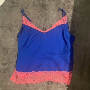 Blå linnetopp med rosa spets- Gina tricot - Snygg blå linnetopp med tunna axelband och detaljer i rosa spets längs halsringning och nederkant. Perfekt för att lyfta vilken outfit som helst med en färgklick och cool kontrast. Lätt och luftig känsla.