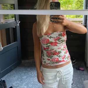 Blommig tubtopp i vitt och rosa - Säljer en söt tubtopp med blommigt mönster i rosa och rött på vit botten. Toppen är ärmlös och har en tight passform, perfekt för sommardagar!!💕Xs-s!