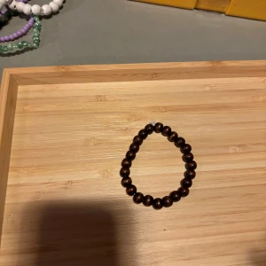 Brunt pärlarmband - Snyggt armband med runda, bruna pärlor trädda på elastisk tråd. Perfekt accessoar för att ge din outfit en naturlig och stilren touch. Passar de flesta handleder tack vare stretch.