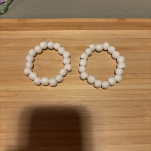 12kr/st Vita pärlarmband - (12kr/st) Två elastiska armband med stora vita pärlor. Perfekta som accessoar för att ge en stilren och fräsch touch till din outfit. Passar både till vardags och när du vill piffa till det lite extra.