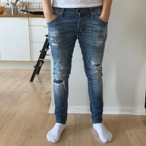 Blå slitna jeans med skinny fit - Säljer ett par blå jeans med skinny passform och slitna detaljer på både fram- och baksida. Jeansen har klassisk femficksdesign, dragkedjegylf och är i stretchigt denimtyg. Perfekta för en avslappnad och trendig look. Dm för frågor!