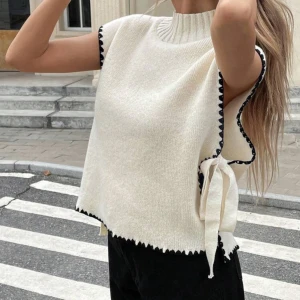 Stickad topp - Beige stickad ärmlös topp med svarta detaljer längs kanterna och knytband i sidan. Aldrig använd!