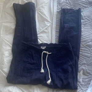Mörkblå linnebyxor från Roxy med snörning - Säljer ett par mörkblå linnebyxor från Roxy med vit snörning i midjan och fickor både fram och bak. Byxorna har en avslappnad passform och är perfekta för varma dagar.