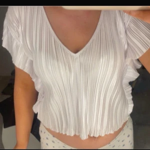 Vit plisserad croppad blus - Säljer en vit plisserad blus med v-ringning och korta volangärmar. Toppen är croppad och har en luftig och flowy känsla, perfekt för varma dagar.