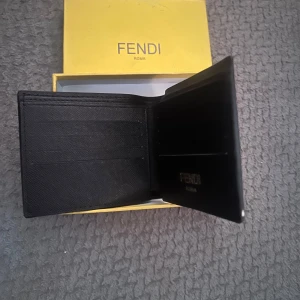 Svart plånbok från Fendi med ögonmotiv - Säljer en svart plånbok från Fendi med coola ögonmotiv i gult och vitt på framsidan. Plånboken har flera kortfack och levereras i original ask. Perfekt accessoar för dig som vill sticka ut.
