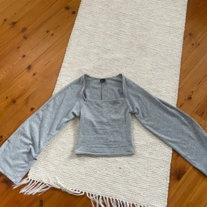 Grå långärmad topp från Gina Tricot - Säljer en ljusgrå långärmad topp från Gina Tricot i storlek XS. Toppen har en fyrkantig urringning och är gjord i mjukt, stretchigt material. Perfekt för en stilren och enkel look.