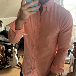 Korallfärgad skjorta från Ralph Lauren - Säljer en snygg korallfärgad skjorta från Ralph Lauren med klassisk broderad logga på bröstet. Skjortan har lång ärm, knappar hela vägen och button-down krage. Perfekt för dig som gillar stilrena plagg med en sportig touch.
