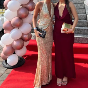 Glittrig långklänning med djup v-ringning - Säljer en glittrig långklänning i champagnefärg med djup v-ringning och halterneck. Klänningen har figurnära passform och är perfekt för festliga tillfällen. Materialet är glittrigt och skimrande, vilket ger en lyxig känsla.