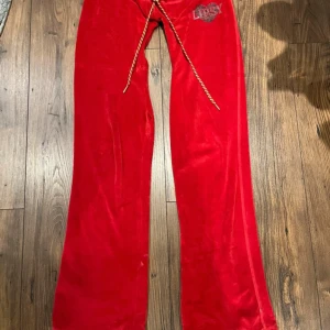 Röda velourbyxor från Lipsy med snörning och matchande tröja - Säljer ett par röda velourbyxor från Lipsy med snörning i midjan och utsvängda ben. Byxorna säljs med en matchande tröja. Går att köpa separat om det skulle önskas 