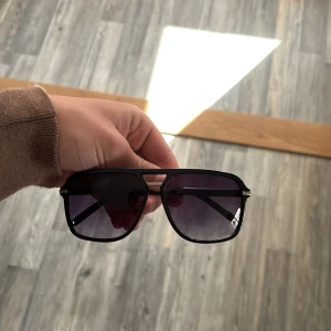 Svarta solglasögon med fyrkantig form - Stilrena svarta solglasögon med markerad fyrkantig båge och mörka linser. Snygg och modern design som passar till många outfits. Bågarna är i plast och har en klassisk look.