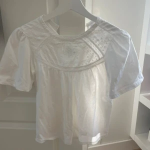 Vit blus med broderade detaljer från Zara  - Söt vit blus med korta puffärmar och broderade detaljer framtill. Rund halsringning och knäppning i nacken. Perfekt för en fräsch och somrig look!😎😙💞