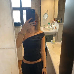 Svart one shoulder topp - Säljer en svart, tight one shoulder topp med snygg drapering. Toppen är croppad och har en stilren, asymmetrisk design som passar perfekt till många olika outfits.