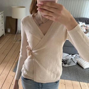 Beige omlottstickad tröja från Flash Woman - Säljer en beige stickad omlott-tröja från Flash Woman i storlek S. Tröjan har lång ärm, knytning i sidan och ett diskret strukturmönster. Perfekt för lager-på-lager och enkel att matcha med jeans eller kjol. Pris går att diskutera💗
