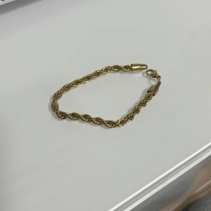 Guld cordell armband - Säljer ett snyggt armband i guldfärg med tvinnad kedja. Perfekt accessoar för att lyfta din outfit med en elegant touch. Lätt att matcha med andra smycken och passar de flesta handleder. (Guld pläterat)