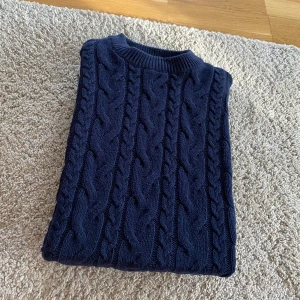 Mörkblå kabelstickad tröja - Mysig mörkblå kabelstickad tröja med rund halsringning och grovstickat mönster. Perfekt för kyligare dagar och passar till många olika outfits. Klassisk och tidlös design.