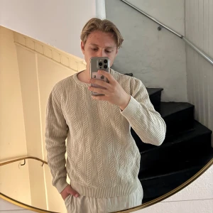 Beige stickad tröja från Dressmann - Säljer en beige stickad tröja från Dressmann i storlek M. Tröjan har ett klassiskt kabelstickat mönster och rund halsringning. Perfekt för lager-på-lager och enkel att matcha med olika outfits.