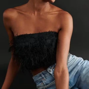 Svart fjädrig tubtopp - Säljer en svart tubtopp med fjäderliknande detaljer. Stretchig smock och dragkedja bak. 