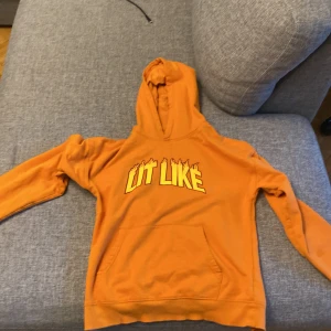 Orange hoodie med tryck 'LIT LIKE' - Säljer en orange hoodie från Cubus med trycket 'LIT LIKE' i gult med eld-detaljer på bröstet. Tröjan har huva och en stor magficka framtill. Perfekt för dig som gillar färg och statement-plagg!