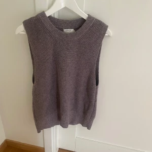 Stickad väst från ONLY i lila - Säljer en stickad väst från ONLY i en mjuk lila nyans. Västen har en rund halsringning och ribbade kanter vid hals och nederkant. Perfekt att styla över en skjorta eller t-shirt för en trendig lager-på-lager-look.