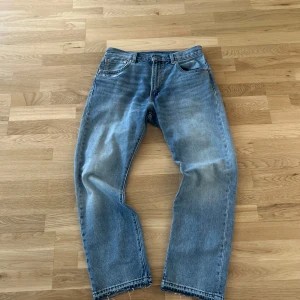Levis 551 blå jeans W32 L30 - Klassiska blå Levis 551 jeans med rak passform och råa, avklippta benslut. Jeansen har fem fickor, knappgylf och är i en ljusblå tvätt. Perfekta för en avslappnad och tidlös stil.