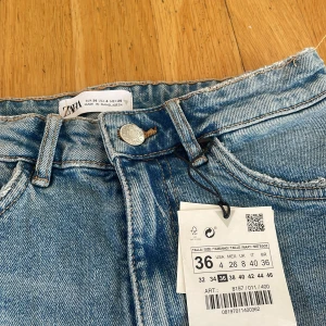 Blå jeansshorts med fransar från Zara - Säljer ett par blå jeansshorts från Zara i klassisk femficksmodell. Shortsen har råa, fransiga benslut och hög midja. Perfekta för sommaren och lätta att matcha med olika toppar.