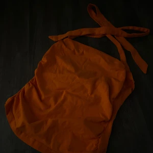 Orange topp med knytband - Säljer en orange sommartop i stretchig material. Toppen har en enkel, ärmlös design och är tillverkad i ett mjukt tyg som känns bekvämt mot huden. Perfekt för varma dagar när du vill ha något färgstarkt och stilrent.