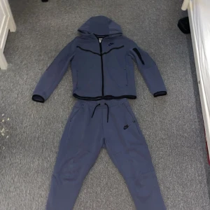 Blå hoodiejacka från Nike - Säljer Nike Tech Tracksuit (Tröjan & Byxorna) då de är för små för mig. Storlek 147-158cm (XS) Använts få tal gånger. Inga deffekter. ÄKTA!! Pris kan diskuteras. Färgen är blå.