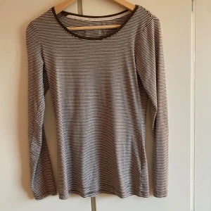 Randig långärmad tröja från H&M - Säljer en klassisk långärmad tröja från H&M med smala svarta och vita ränder. Tröjan har rund halsringning och är i mjuk bomull, perfekt för lager-på-lager eller som den är.